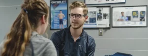 a chiropractor in cochrane carefully discussing treatment options with a focused athlete, surrounded by posters highlighting various sports injuries.