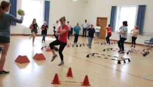 A group of people performing various coordination exercises in a bright, well-lit gymnasium. In the foreground, individuals are engaged in activities such as balancing on one leg, throwing and catching balls, and navigating through agility ladders. The middle ground features participants executing more complex movements, like hopping on one foot or weaving through a series of cones. In the background, a coach or therapist observes and provides guidance, with the overall scene conveying a sense of focused, collaborative effort towards improving coordination and balance.